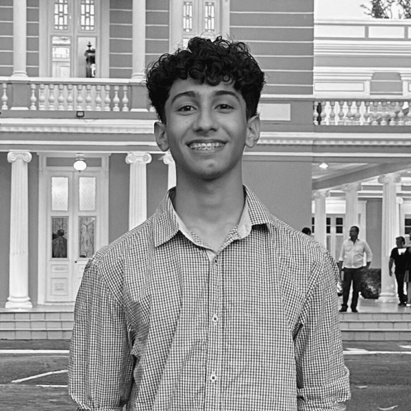 Foto em preto e branco de Luiz, jovem com cabelo curto e com cachos, sorrindo para a foto, usando uma camisa social xadrez