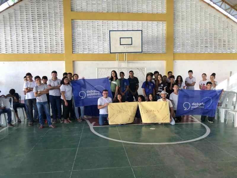 Um grupo de jovens reunidos segurando a bandeira dos Debates Públicos das Escolas