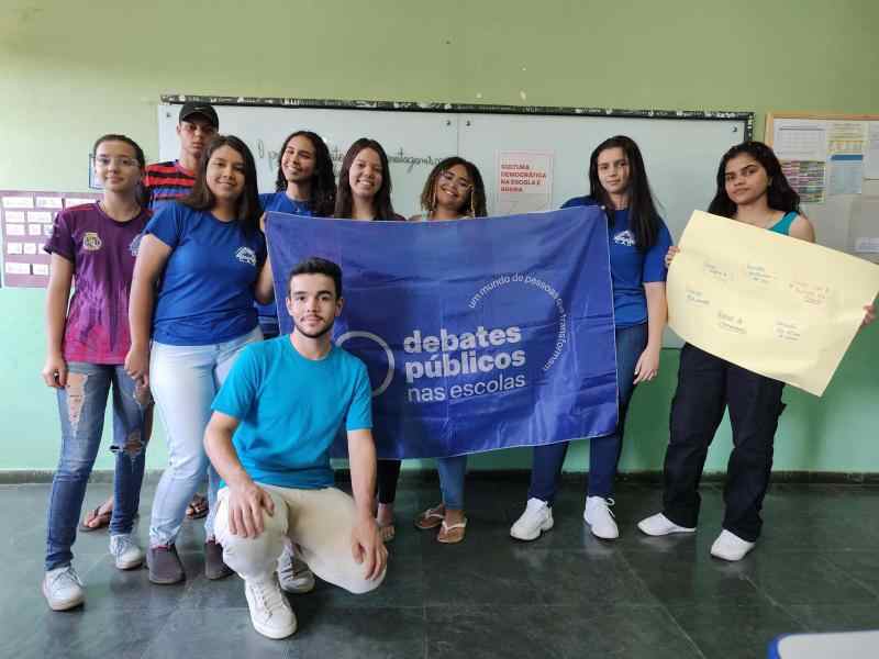 Um grupo de jovens reunidos segurando a bandeira dos debates públicos nas escolas