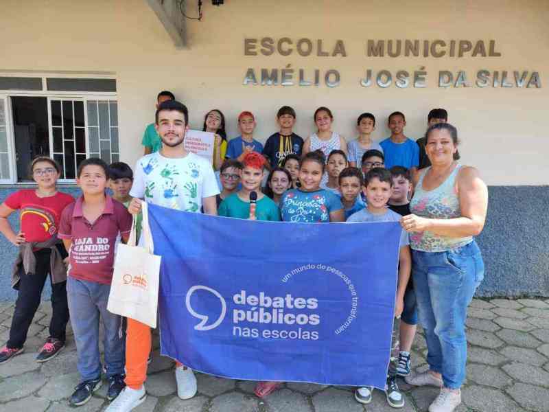 Um grupo de jovens reunidos segurando a bandeira dos Debates Públicos das Escolas