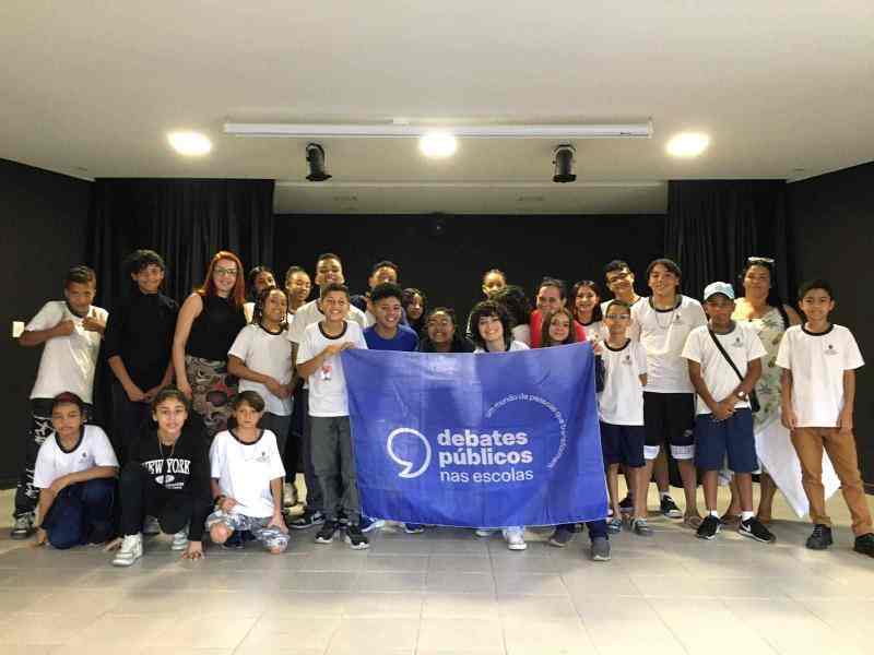 Um grupo de jovens reunidos segurando a bandeira dos Debates Públicos das Escolas