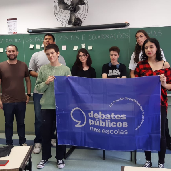 Um grupo de jovens reunidos segurando a bandeira dos Debates Públicos das Escolas