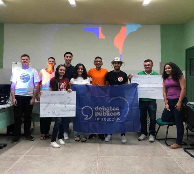 Um grupo de jovens reunidos segurando a bandeira dos Debates Públicos das Escolas