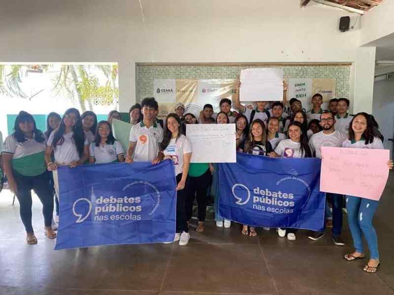 Um grupo de jovens reunidos segurando a bandeira dos Debates Públicos das Escolas