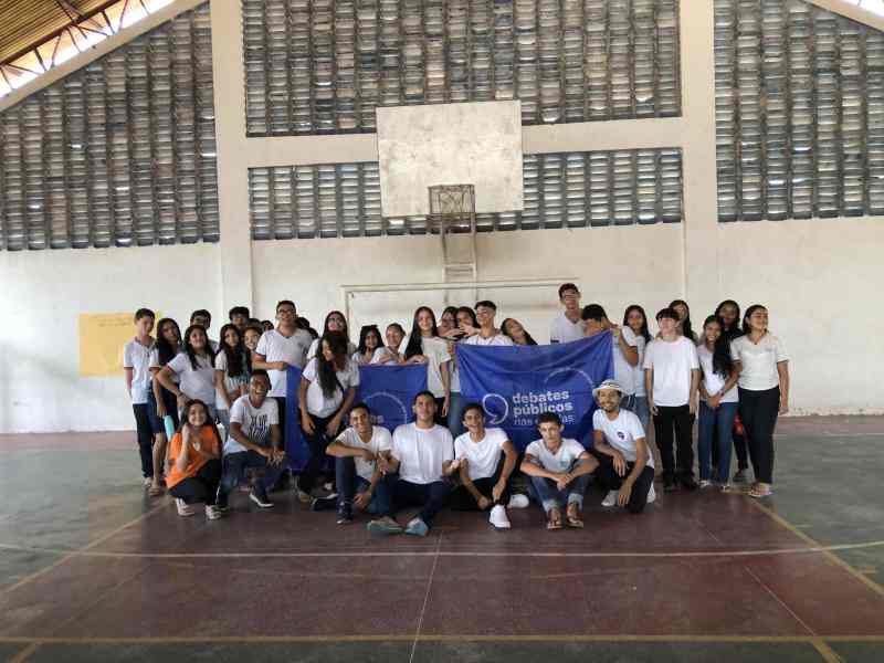 Um grupo de jovens reunidos segurando a bandeira dos Debates Públicos das Escolas