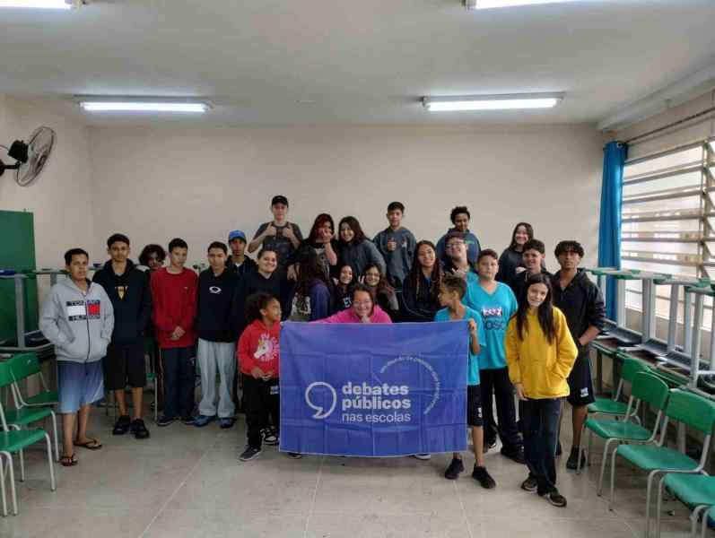 Um grupo de jovens reunidos segurando a bandeira dos Debates Públicos das Escolas