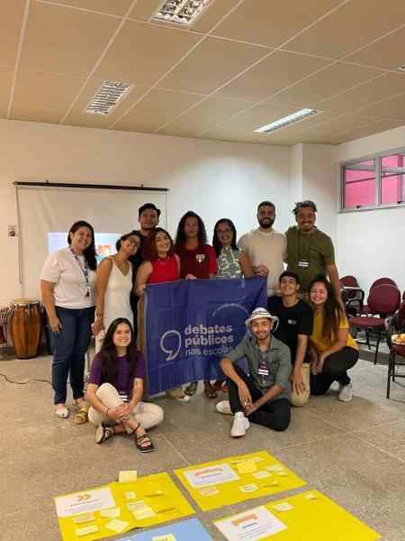 Um grupo de jovens reunidos segurando a bandeira dos Debates Públicos das Escolas