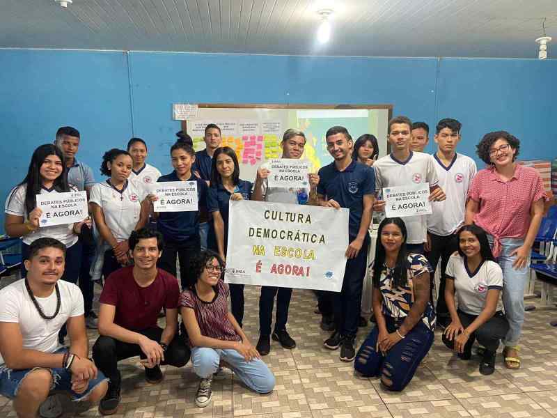 Grupo de jovens reunidos em uma sala seguram cartazes sobre cultura democrática