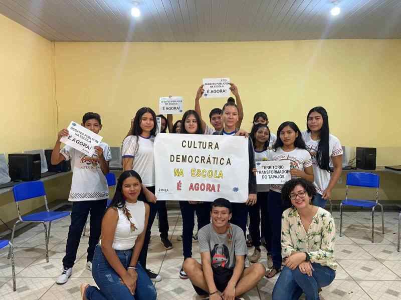 Grupo de jovens em uma sala de aula seguram cartazes sobre cultura democrática