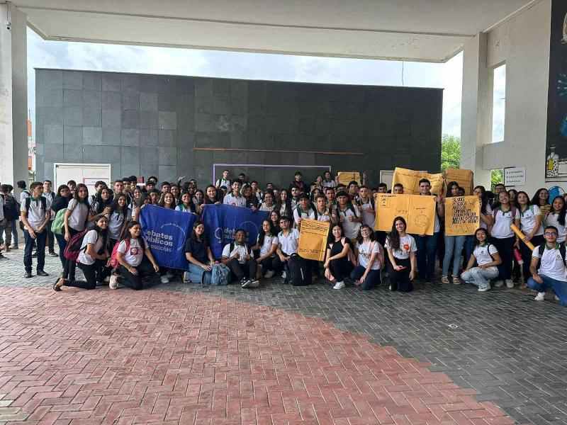 Um grupo de pessoas reunidos segurando a bandeira dos Debates Públicos das Escolas