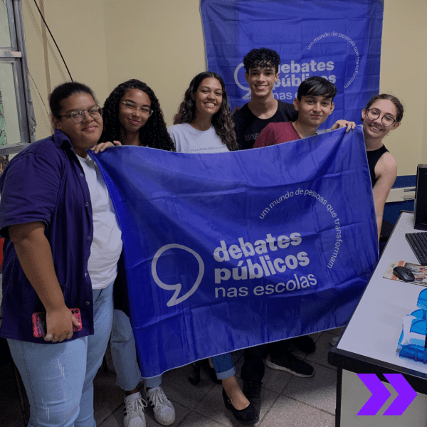 Um grupo de pessoas reunidos segurando a bandeira dos Debates Públicos das Escolas