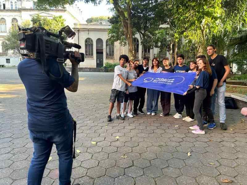  o pátio escola e alguns estudantes segurando a bandeira dos debates públicos nas escolas enquanto um homem os grava com uma câmera nos ombros