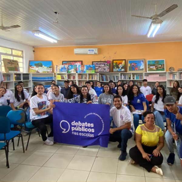 Um grupo de pessoas reunidos segurando a bandeira dos Debates Públicos das Escolas