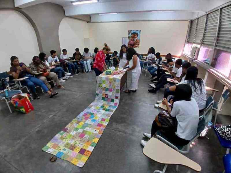 um grupo de mulheres em circulo ao redor de uma colcha de retalhos no centro da sala.