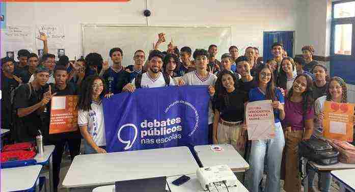 Um grupo de jovens reunidos segurando a bandeira dos Debates Públicos das Escolas