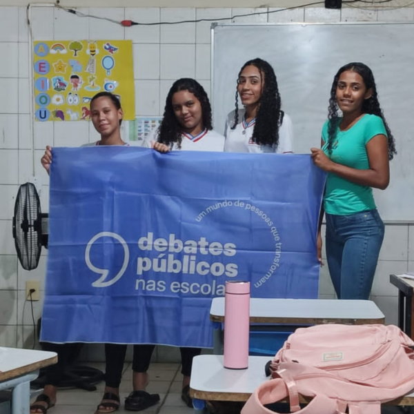 Um grupo de pessoas reunidos segurando a bandeira dos Debates Públicos das Escolas