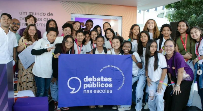 Um grupo de pessoas reunidos segurando a bandeira dos Debates Públicos das Escolas