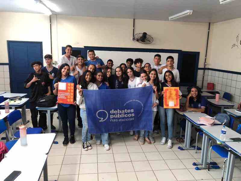 Um grupo de jovens reunidos segurando a bandeira dos Debates Públicos das Escolas