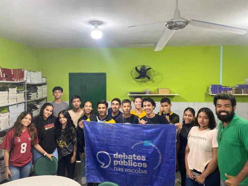 Um grupo de pessoas reunidos segurando a bandeira dos Debates Públicos das Escolas