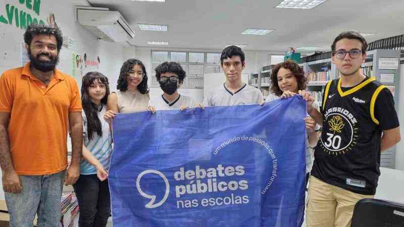 Um grupo de pessoas reunidos segurando a bandeira dos Debates Públicos das Escolas