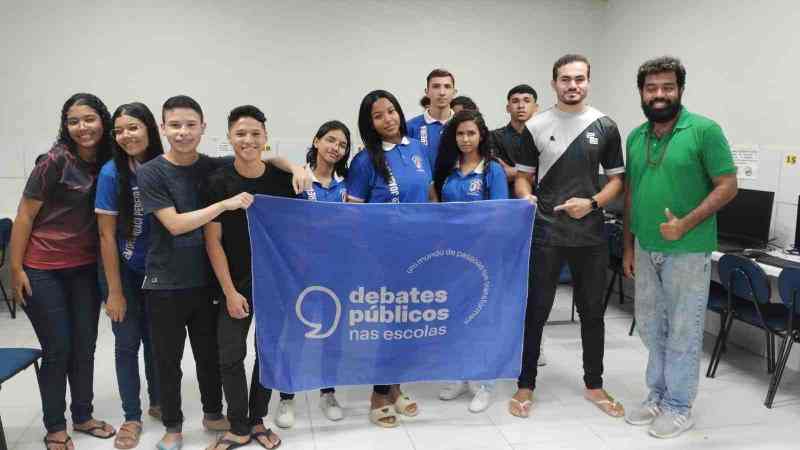 Um grupo de pessoas reunidos segurando a bandeira dos Debates Públicos das Escolas