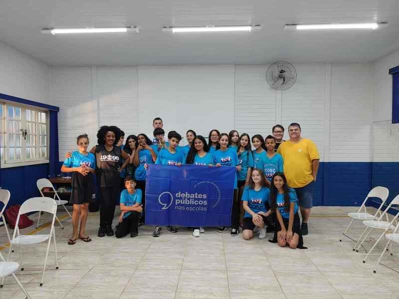 Um grupo de jovens reunidos segurando a bandeira dos Debates Públicos das Escolas