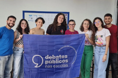 Um grupo de jovens reunidos segurando a bandeira dos Debates Públicos das Escolas