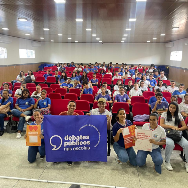 Um grupo de pessoas reunidos segurando a bandeira dos Debates Públicos das Escolas