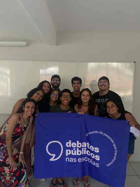 Um grupo de jovens reunidos segurando a bandeira dos Debates Públicos das Escolas