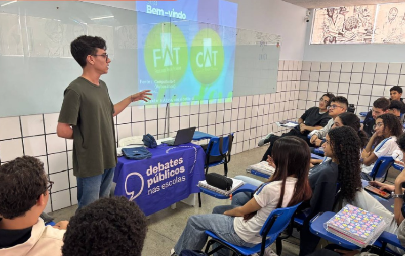 Um grupo de jovens reunidos sentados em sala de aula assistindo a Nathan falar