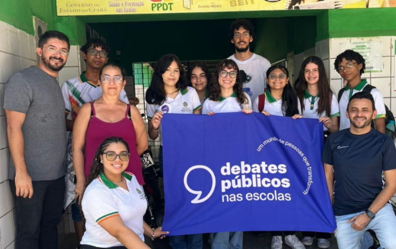 Um grupo de jovens reunidos segurando a bandeira dos Debates Públicos das Escolas