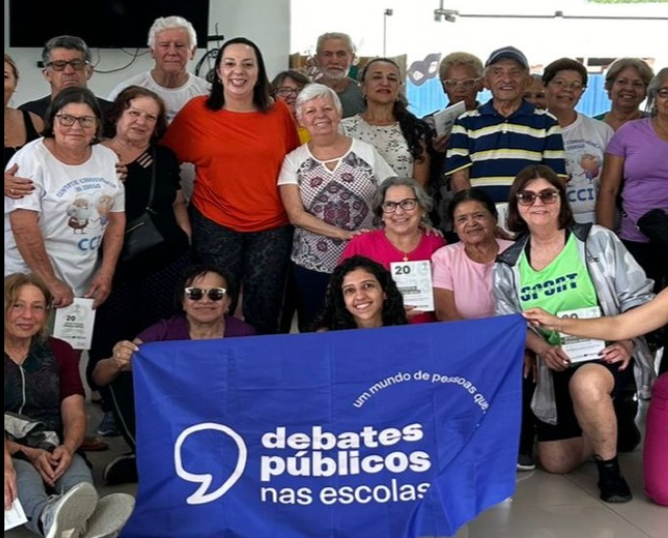 Um grupo de pessoas reunidas segurando a bandeira dos Debates Públicos das Escolas