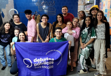 Um grupo de jovens reunidos segurando a bandeira dos Debates Públicos das Escolas