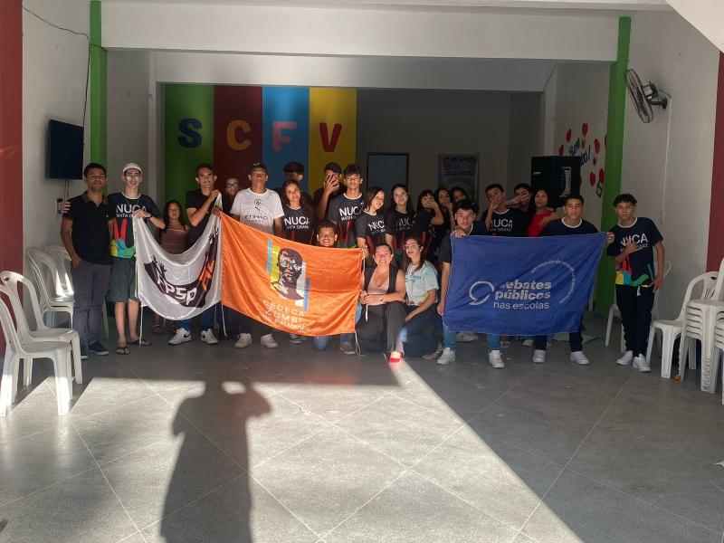 Grupo de pessoas reunidas com duas bandeiras nas mãos.