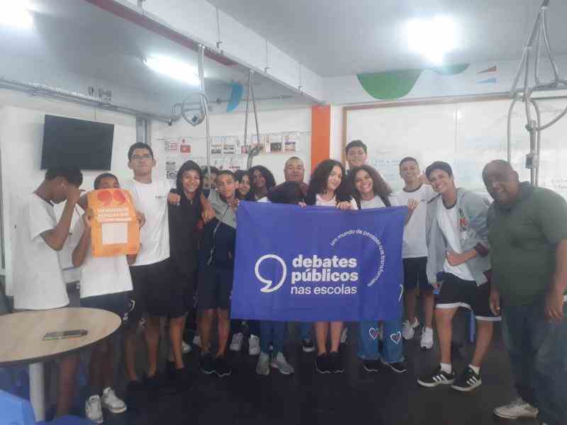 Grupo de jovens reunidos em um sala, uma bandeira dos Debates Publicos Nas Escolas exibida pelas pessoas .
