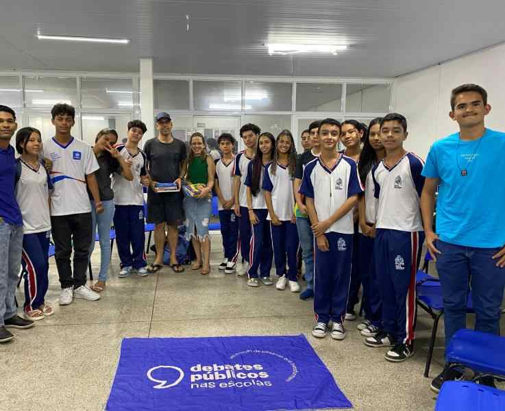 Grupo de jovens reunidos em um sala, uma bandeira dos Debates Publicos Nas Escolas estendida sob o chão.