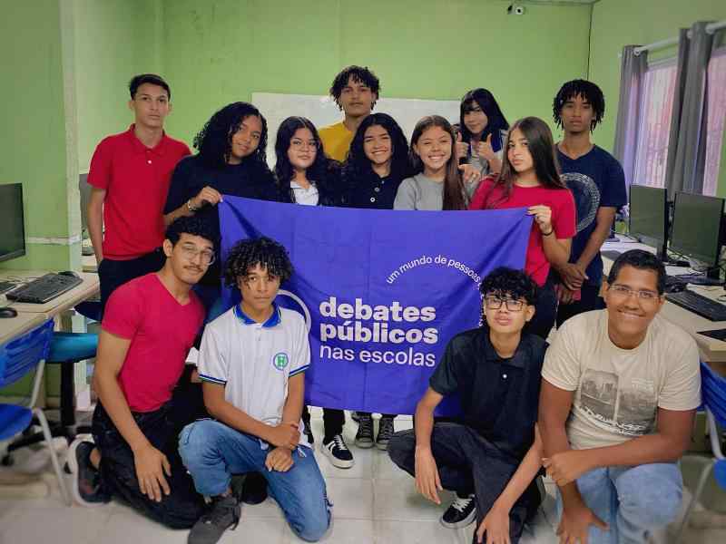 Grupo de jovens reunidos em um sala, uma bandeira dos Debates Publicos Nas Escolas estendida sob o chão.
