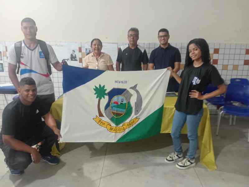 Grupo de jovens reunidos em um sala, uma bandeira do municipio de Rio das Pedras em Destaque.
