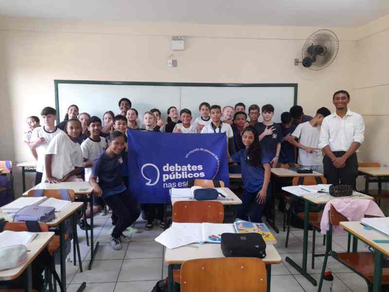 Grupo de jovens reunidos em um sala, uma bandeira dos Debates Publicos Nas Escolas estendida sob o chão.