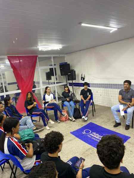 Grupo de jovens reunidos em um sala, uma bandeira dos Debates Publicos Nas Escolas estendida sob o chão.