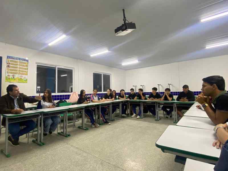 Grupo de jovens reunidos em um sala, uma bandeira dos Debates Publicos Nas Escolas estendida sob o chão.