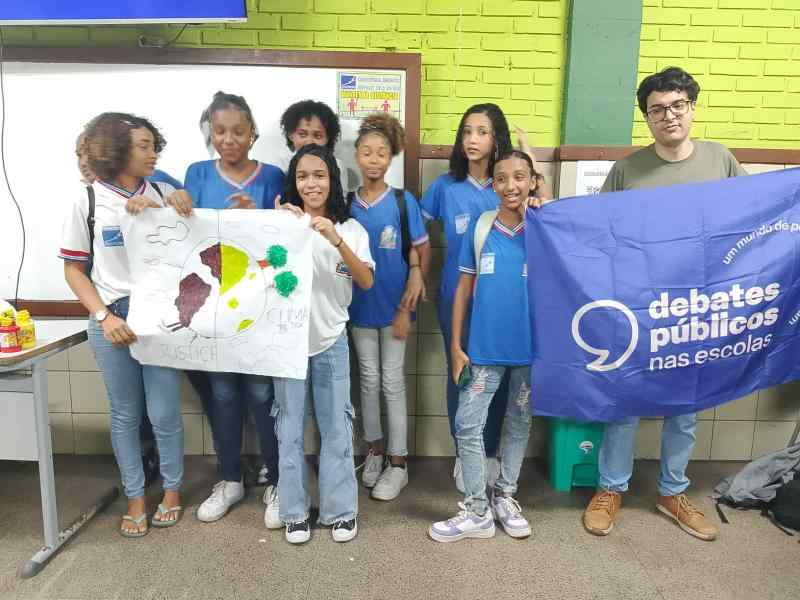 Grupo de jovens reunidos em um sala, uma bandeira dos Debates Publicos Nas Escolas estendida sob o chão.