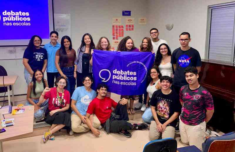 Grupo de jovens reunidos em um sala, uma bandeira dos Debates Publicos Nas Escolas estendida sob o chão.