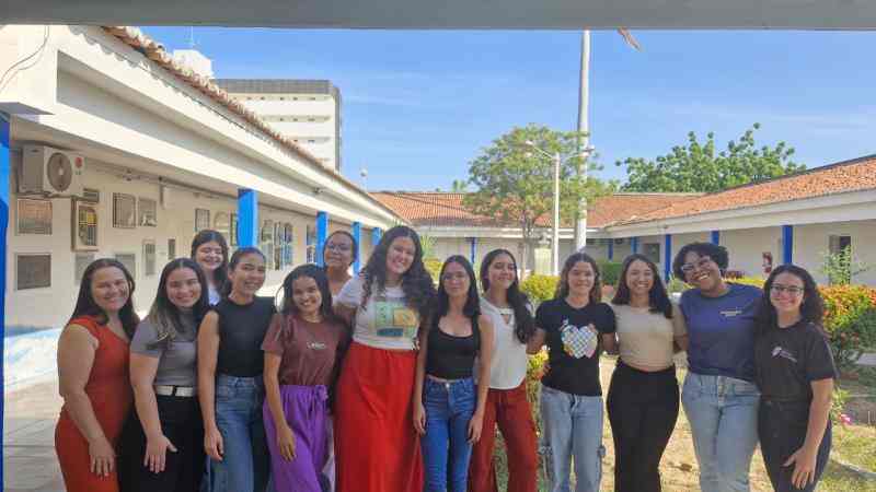 Grupo de jovens reunidos em um sala, uma bandeira dos Debates Publicos Nas Escolas estendida sob o chão.