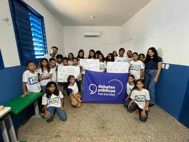 Grupo de jovens reunidos em um sala, uma bandeira dos Debates Publicos Nas Escolas estendida sob o chão.