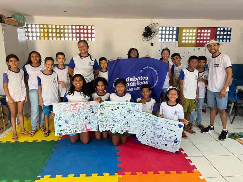 Grupo de jovens reunidos em um sala, uma bandeira dos Debates Publicos Nas Escolas estendida sob o chão.