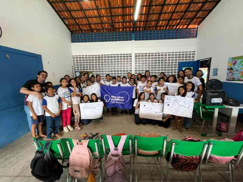 Grupo de jovens reunidos em um sala, uma bandeira dos Debates Publicos Nas Escolas estendida sob o chão.