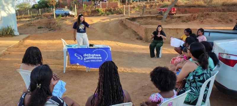 Grupo de jovens reunidos em um sala, uma bandeira dos Debates Publicos Nas Escolas estendida sob o chão.