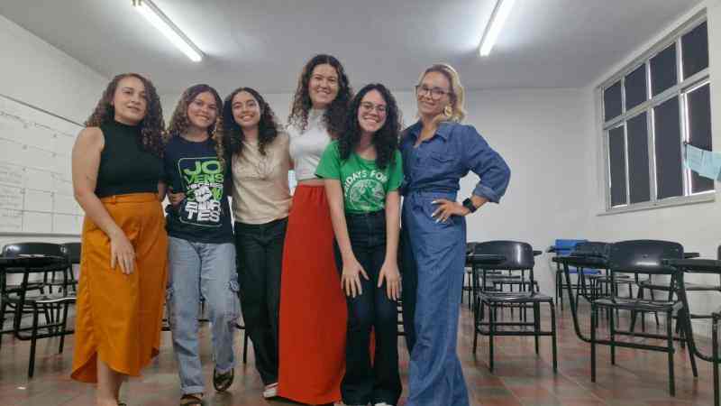 Grupo de jovens reunidos em um sala, uma bandeira dos Debates Publicos Nas Escolas estendida sob o chão.