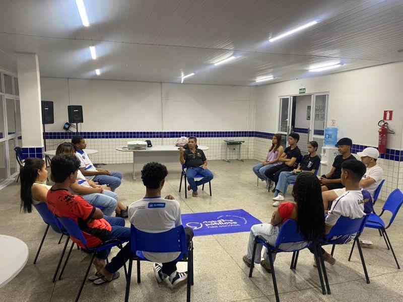 Grupo de jovens reunidos em um sala, uma bandeira dos Debates Publicos Nas Escolas estendida sob o chão.